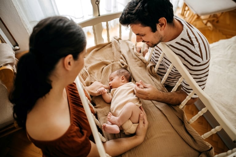 Parents looking at their sleeping baby in a cradle