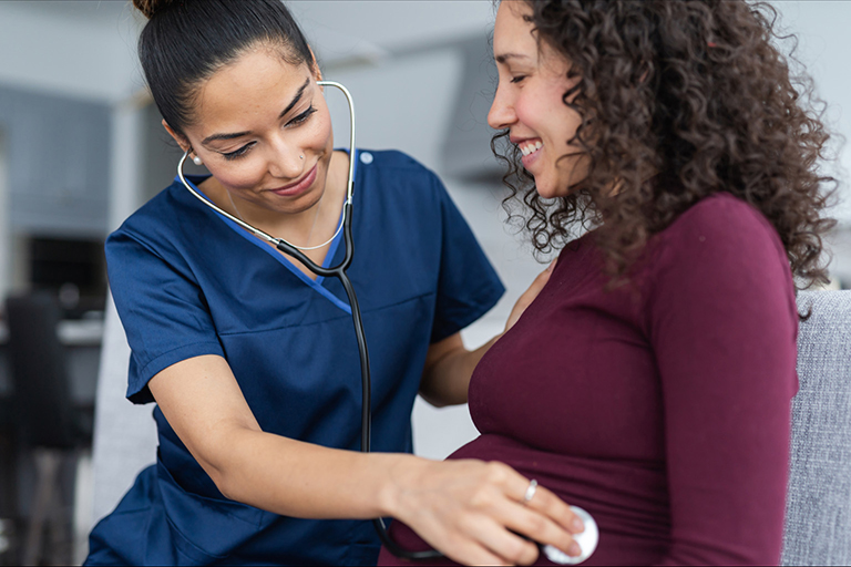 A nurse using a stethoscope on a pregnant women's belly 