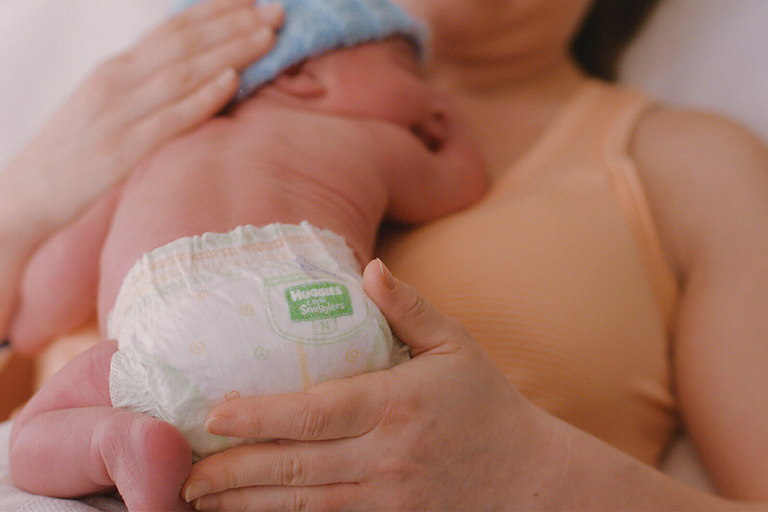 A mother hugging a newborn baby wearing Huggies Diapers