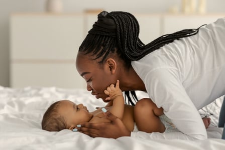 A mother leaning down to kiss her baby lying on the bed