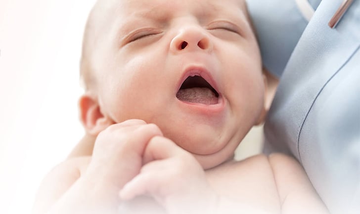 A yawning baby held in nurses' arm