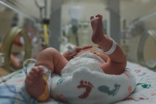 Legs of a diapered baby in NICU on a blanket with footprint design