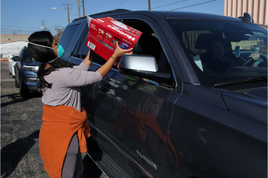 A masked volunteer donating Huggies diaper pack to passengers in a car
