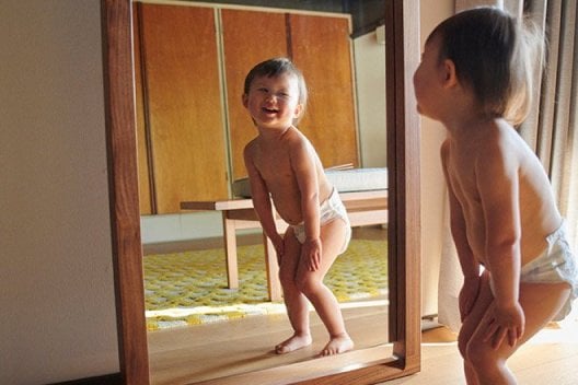 A baby laughs while looking at themselves in a mirror
