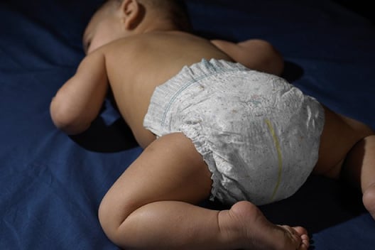 A Diapered baby laying on a dark blue bed sheet.
