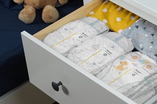 The top drawer of a white dresser is pulled out to display multiple Huggies Overnites Diapers with wetness indicators